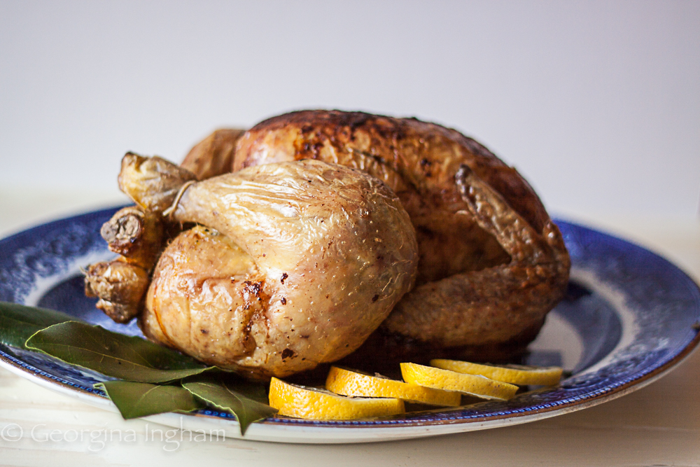 Golden roast chicken with lemon slices and bay leaves on a serving plate &mdash; a traditional herb-roasted chicken prepared with simple aromatics.